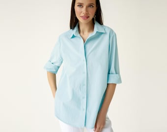 May include: A light blue, long-sleeved button-down shirt with a relaxed fit. The shirt has a collar and a button closure.