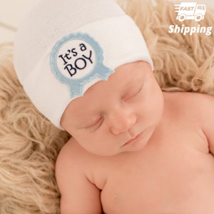 May include: A white knitted baby hat with a blue and white embroidered badge that says "It's a Boy".