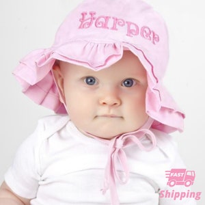 May include: A pink sun hat with a ruffled brim and the name "Harper" embroidered on the front. The hat is tied under the chin with a pink ribbon.