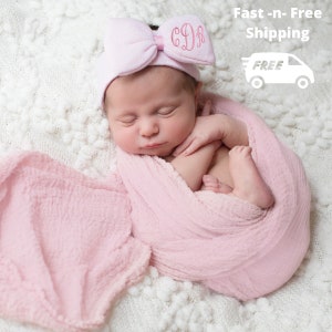 May include: A pink baby headband with a bow and the letters "C.D.R." embroidered on it. The headband is on a baby's head, who is sleeping in a pink swaddle.