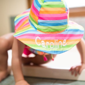May include: A colorful striped sun hat with the name "Caroline" embroidered on the front.