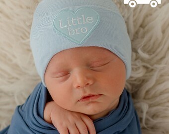 May include: A light blue baby hat with a white heart embroidered with the text "Little bro".