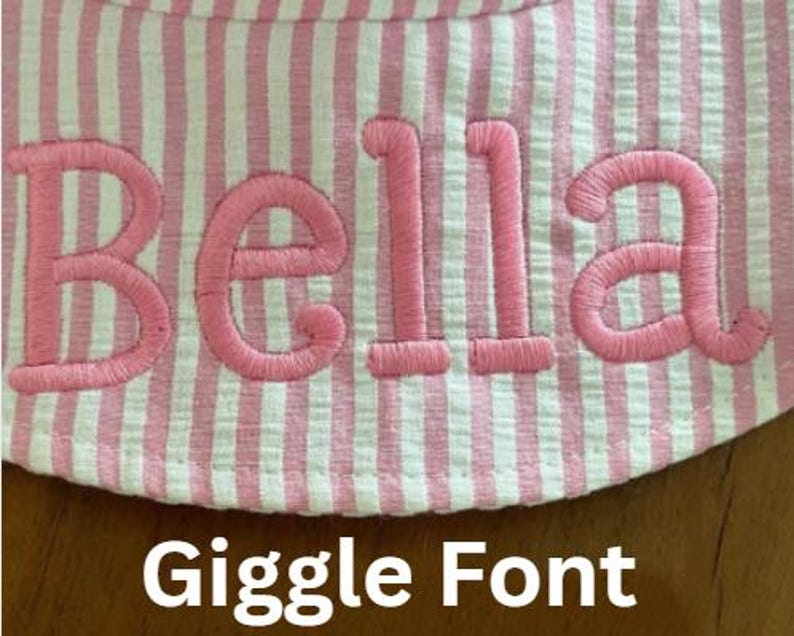 May include: Close-up of a pink and white striped fabric with the name "Bella" embroidered in pink thread. The text "Giggle Font" is displayed below the name. The fabric appears to be part of a hat or similar item.