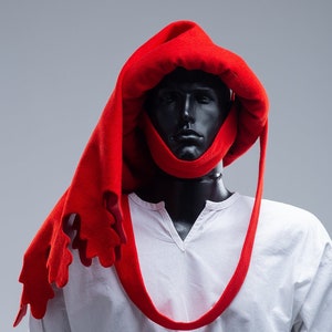 May include: A red hooded cowl with a jagged edge. The cowl is made of a soft, thick fabric and is designed to be worn over the head and neck. The cowl is a medieval-style garment that can be used for cosplay, LARP, or historical reenactment.