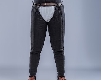 May include: Black padded pants with vertical stitching, worn with a wide, dark gray belt secured by two brown leather straps. The person is wearing a white shirt and brown shoes. The Steel Mastery logo is at the bottom.
