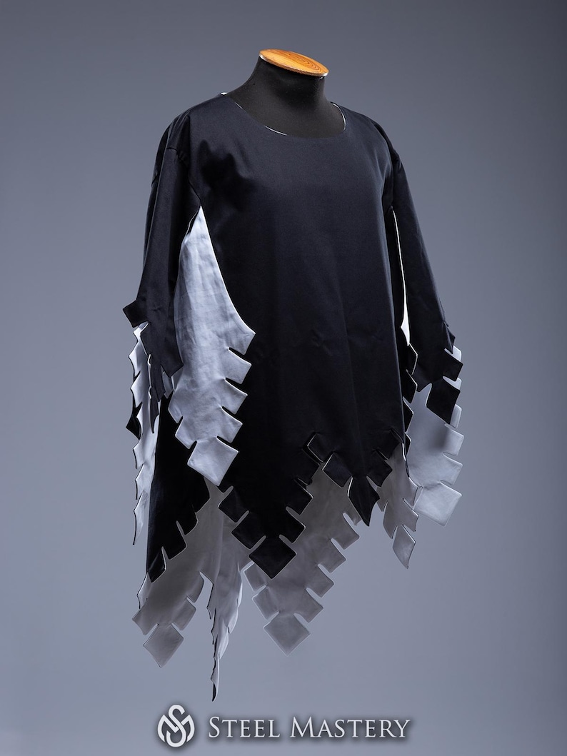 May include: A black tunic with long sleeves and a distinctive design. It has a white panel on the side and a decorative, layered hemline. The hemline is made of alternating black and white geometric shapes.
