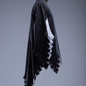 May include: A black garment with white detailing and a distinctive, geometric edge design. The sleeves and hem have a series of rectangular cutouts. The garment is displayed on a mannequin against a grey backdrop. The Steel Mastery logo is visible at the bottom.