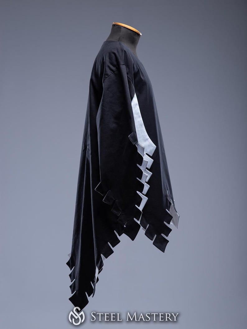 May include: A black garment with white detailing and a distinctive, geometric edge design. The sleeves and hem have a series of rectangular cutouts. The garment is displayed on a mannequin against a grey backdrop. The Steel Mastery logo is visible at the bottom.