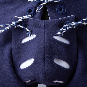 Op de afbeelding: Close-up van de achterkant van een paar donkerblauwe middeleeuwse broeken met witte veters en witte oogjes. De broek heeft een uniek ontwerp met uitsparingen op de rug.