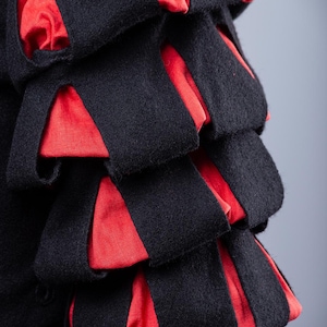 May include: Close-up of a black and red fabric garment with a layered design. The fabric is textured and has a soft appearance.