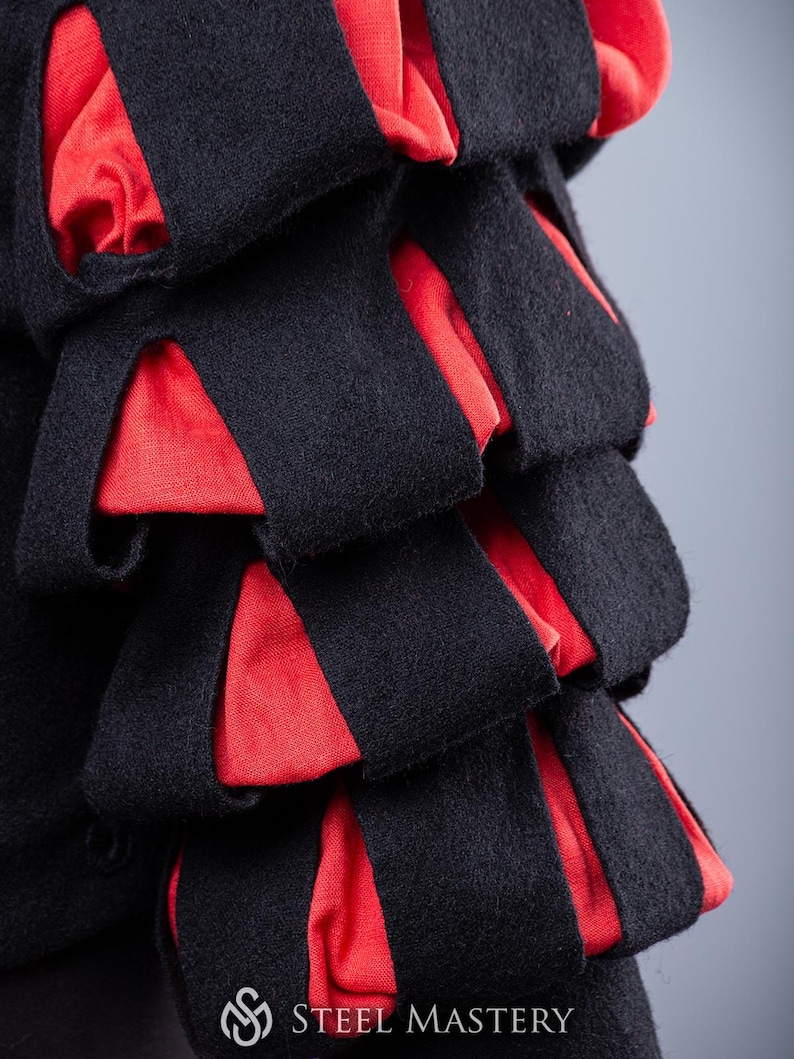 May include: Close-up of a black and red fabric garment with a layered design. The fabric is textured and has a soft appearance.