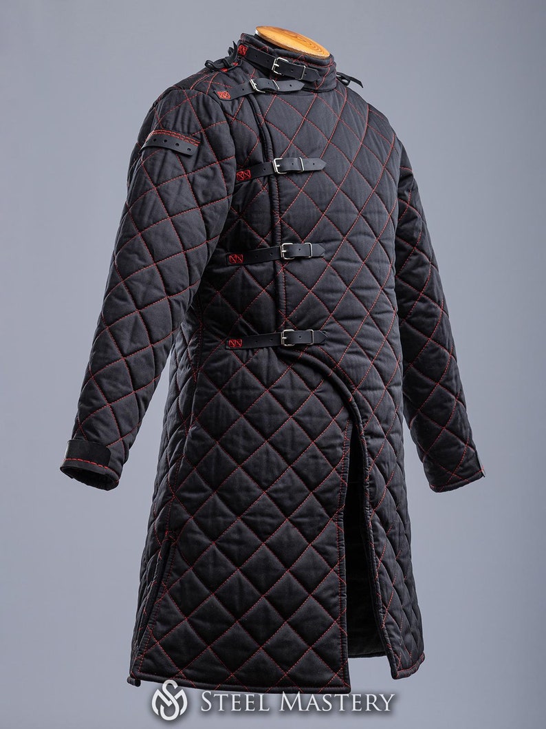 May include: A black quilted jacket with red stitching and multiple straps and buckles. The jacket has a long, fitted style and a high collar.