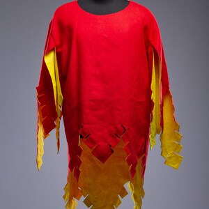 May include: A red tunic with yellow detailing, displayed on a mannequin. The tunic has a round neckline and long sleeves with jagged yellow edges. The hemline also features a jagged yellow design. The Steel Mastery logo is visible.