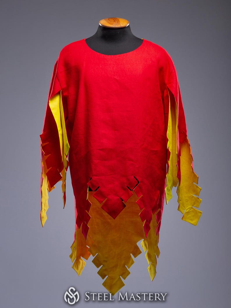 May include: A red tunic with yellow detailing, displayed on a mannequin. The tunic has a round neckline and long sleeves with jagged yellow edges. The hemline also features a jagged yellow design. The Steel Mastery logo is visible.
