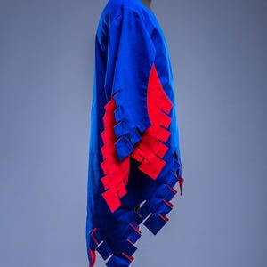 May include: A blue tunic with red detailing, possibly for historical re-enactment. The garment has a long, flowing design with red, rectangular cutouts along the sleeves and hem. The "Steel Mastery" logo is visible at the bottom.