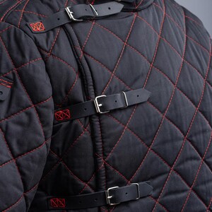 May include: Black quilted jacket with red stitching and leather straps with buckles. The jacket has a high collar and is made of a thick, durable fabric.