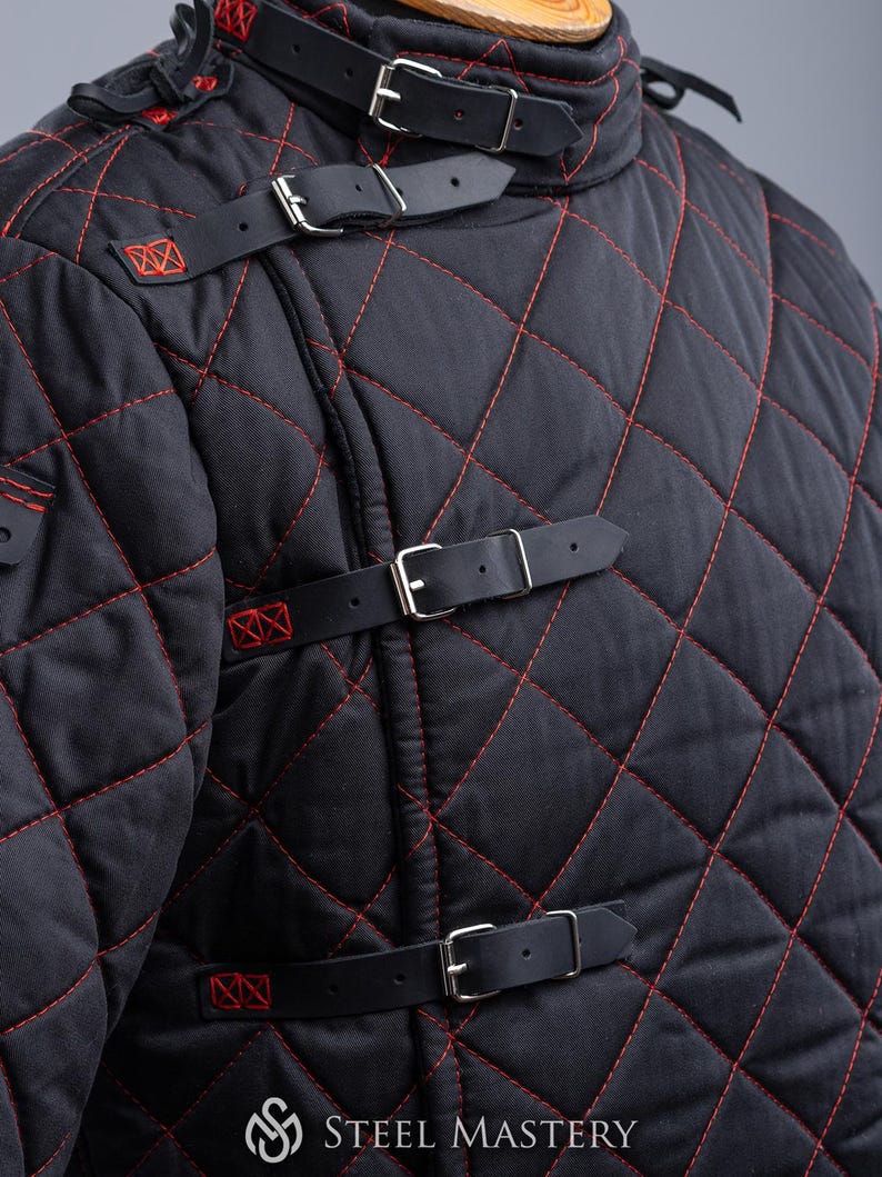 May include: Black quilted jacket with red stitching and leather straps with buckles. The jacket has a high collar and is made of a thick, durable fabric.