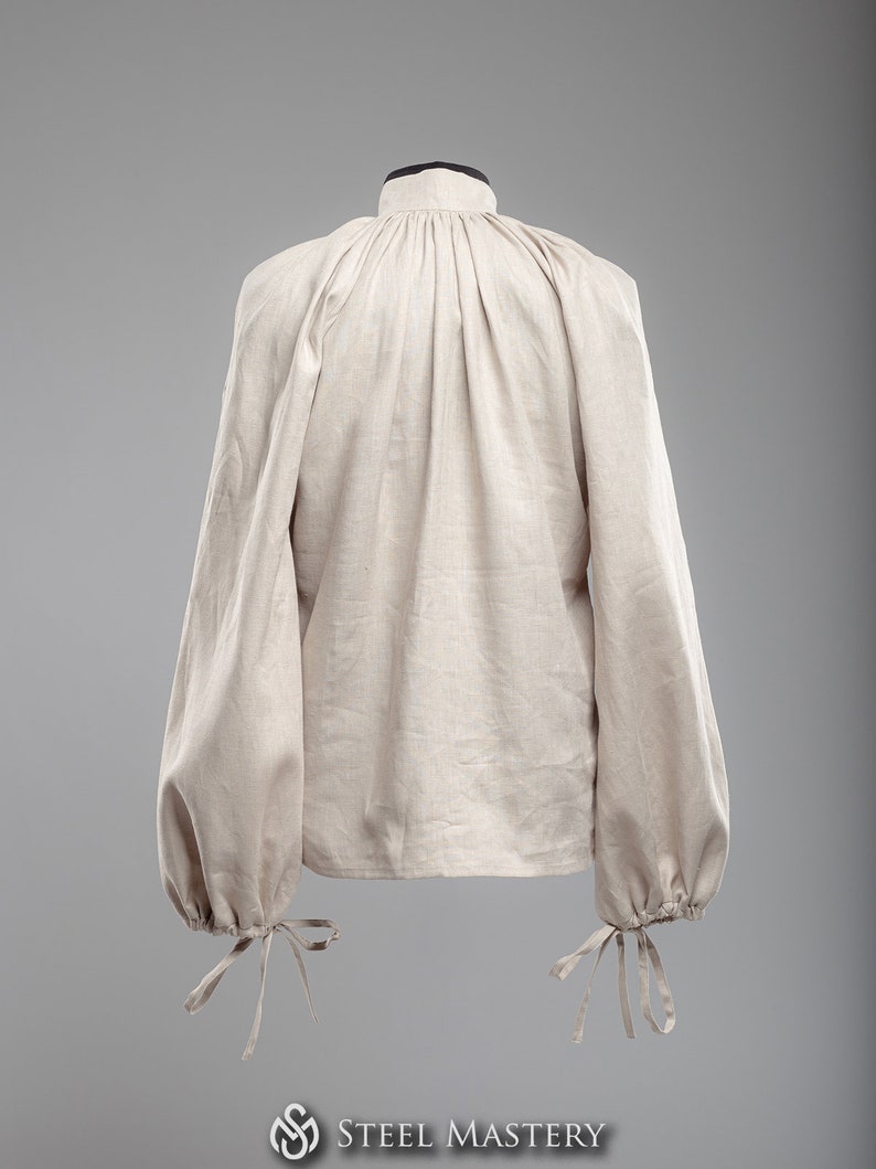 May include: A beige linen shirt with a high collar and long sleeves. The sleeves have gathered cuffs with ties.