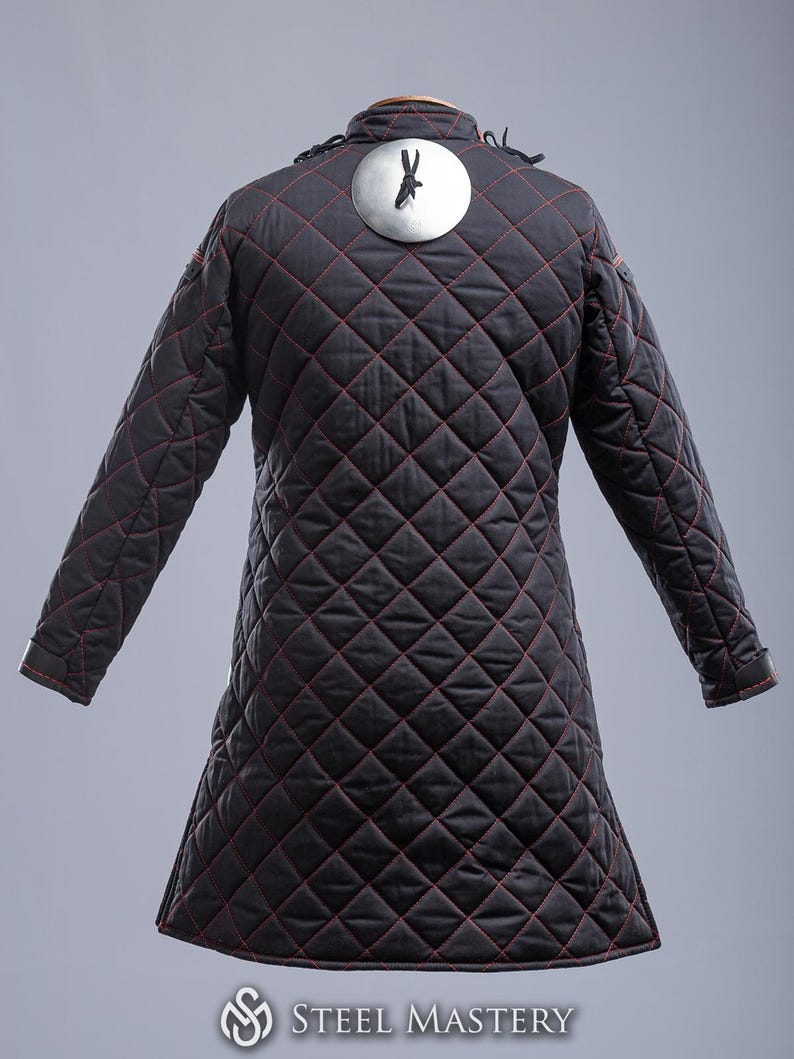 May include: Black quilted jacket with red stitching and a circular metal plate on the back. The plate has a small black design on it.
