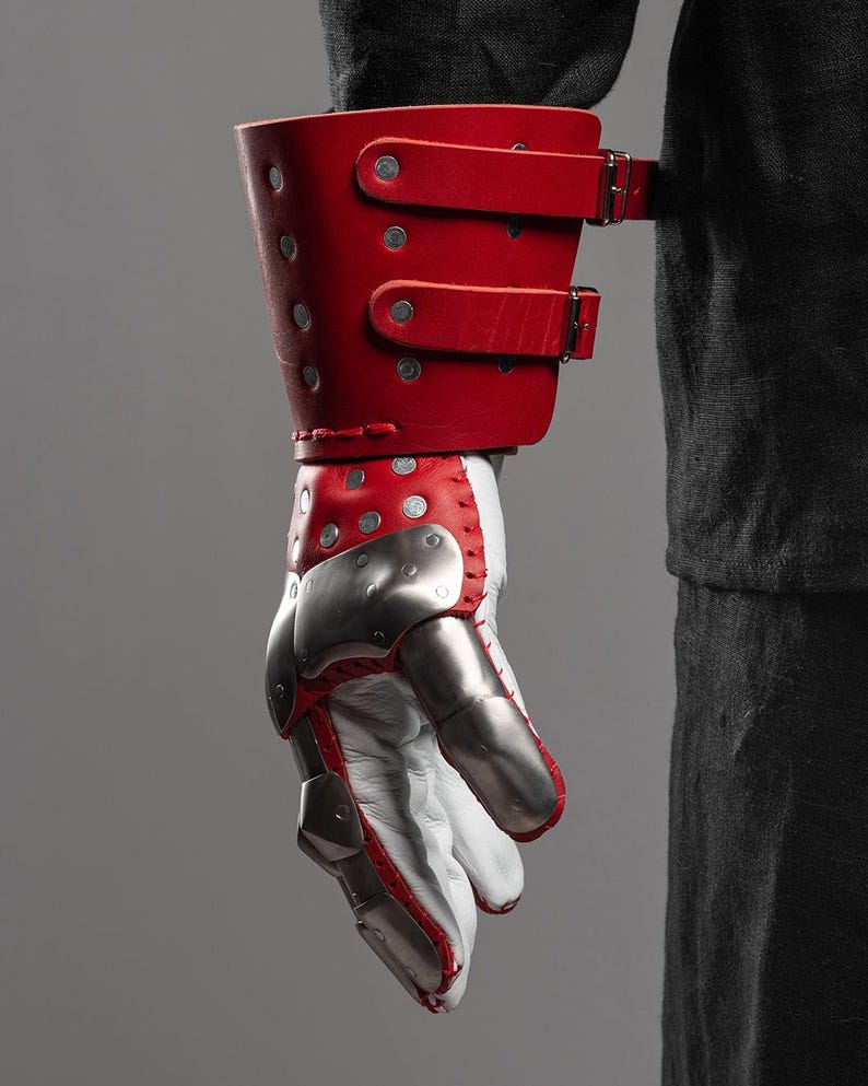 May include: A red leather gauntlet with silver metal plates and white leather. The gauntlet features a red leather cuff with two buckle straps. The hand portion has silver metal plates and red stitching.