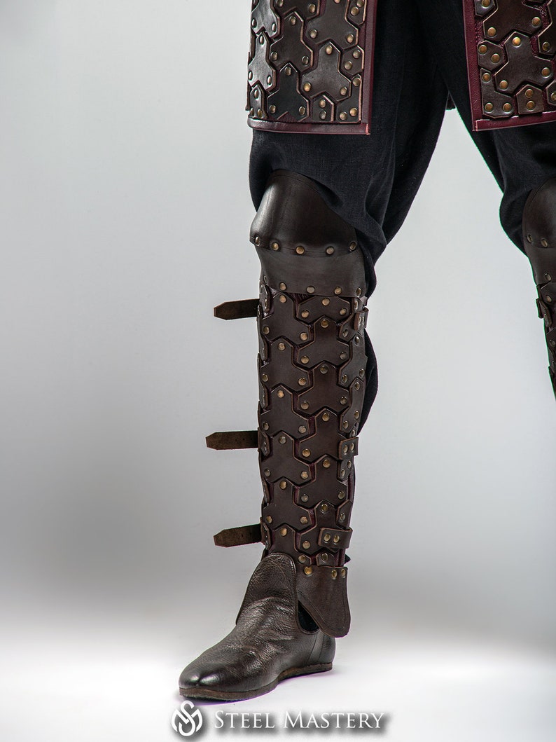May include: Brown leather leg armor with metal accents and buckles. The armor is made of overlapping plates and has a decorative design.
