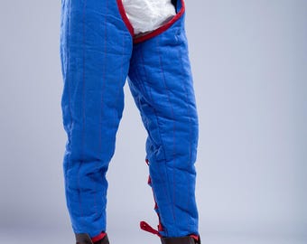 May include: Blue padded pants with red trim and stitching, worn with brown leather boots. The pants have a high waist and are designed for protection. The image shows a close-up of the pants and boots, highlighting the details of the stitching and materials.