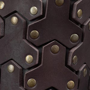 May include: Close-up of a brown leather cuff with a hexagonal pattern and brass rivets. The cuff is made of high-quality leather and is designed to be durable and stylish.