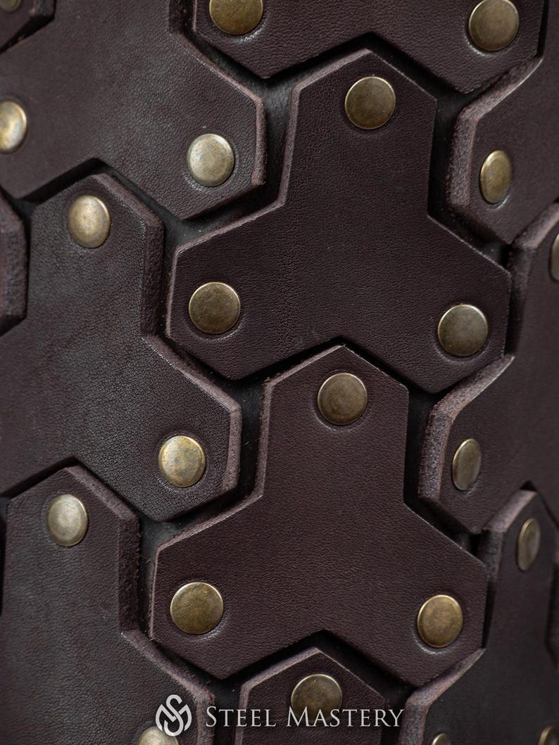May include: Close-up of a brown leather cuff with a hexagonal pattern and brass rivets. The cuff is made of high-quality leather and is designed to be durable and stylish.