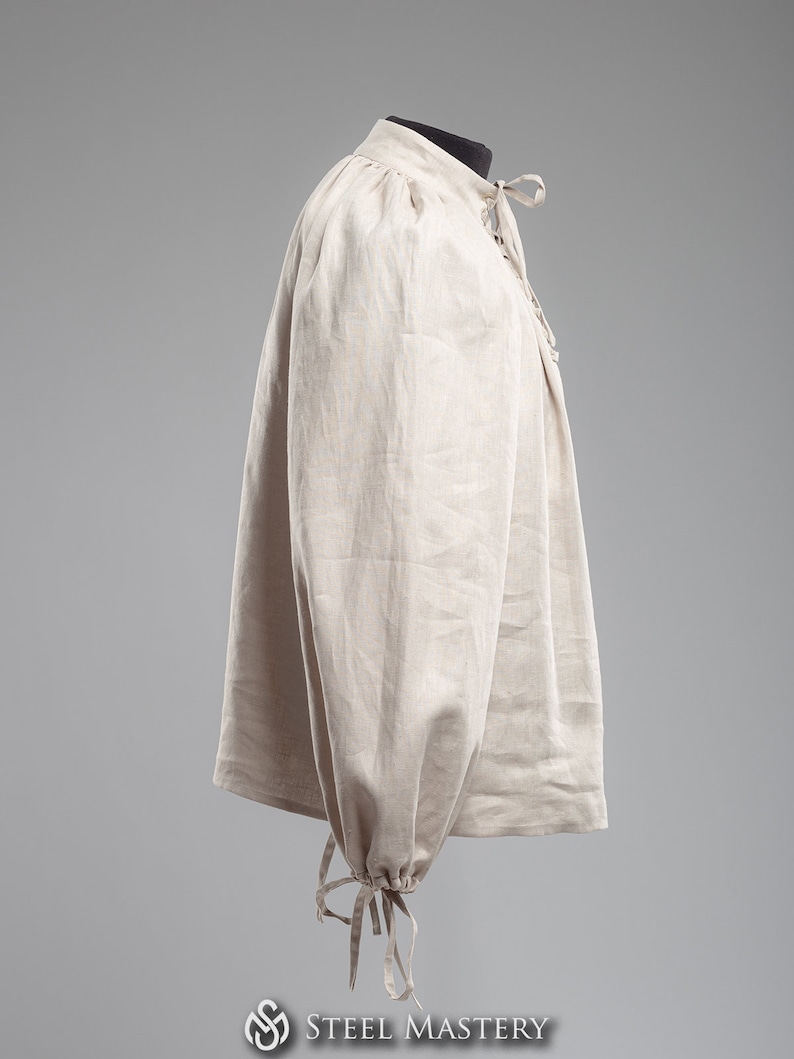 May include: A beige linen shirt with long sleeves and a gathered neckline. The sleeves have a gathered cuff with a tie closure.