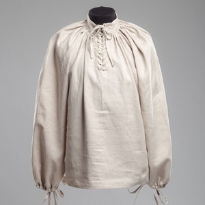May include: A beige linen shirt with a lace-up neckline and long sleeves. The sleeves have ties at the cuffs.