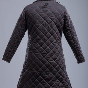 May include: Black quilted jacket with red stitching. The jacket has a high collar and long sleeves. The jacket is made of a thick, durable fabric and is designed for warmth and protection.