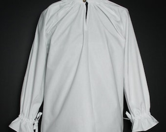 Può includere: Una camicia bianca a maniche lunghe con un colletto arricciato e una chiusura con bottone al collo. La camicia ha maniche a sbuffo con lacci ai polsini.