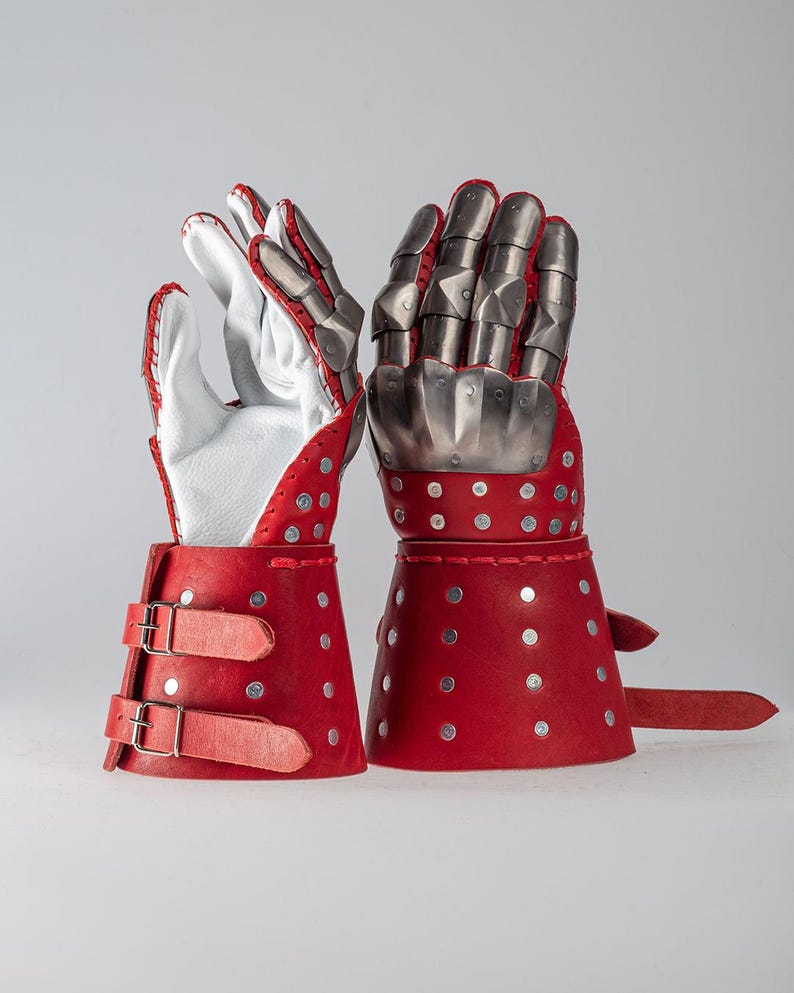 May include: Pair of red and silver medieval gauntlets. The gauntlets feature red leather cuffs with silver rivets and buckles. The hand portion is made of silver metal plates, with white leather gloves inside.