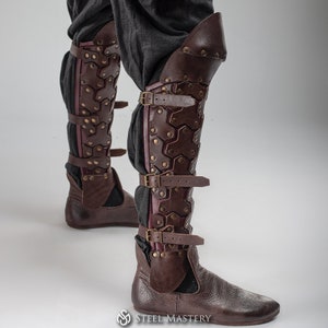 May include: Brown leather knee-high boots with buckles and straps. The boots have a textured, patterned design and are worn over pants.