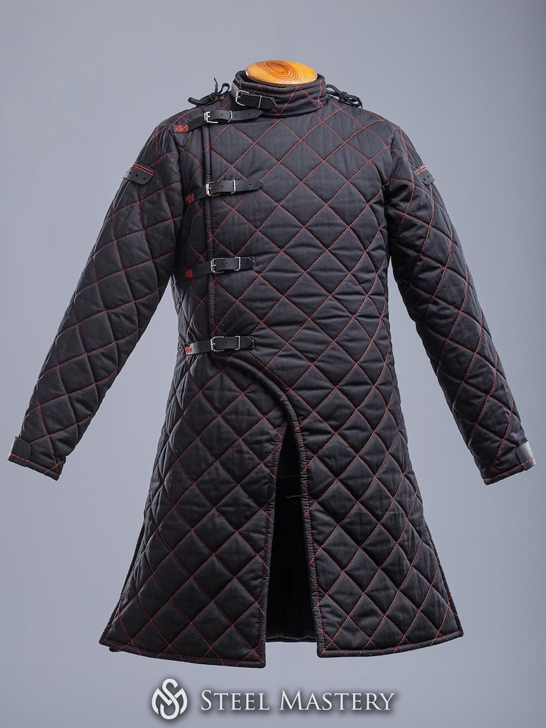 May include: A black quilted jacket with red stitching and multiple buckles. The jacket has a long, fitted style and a high collar.