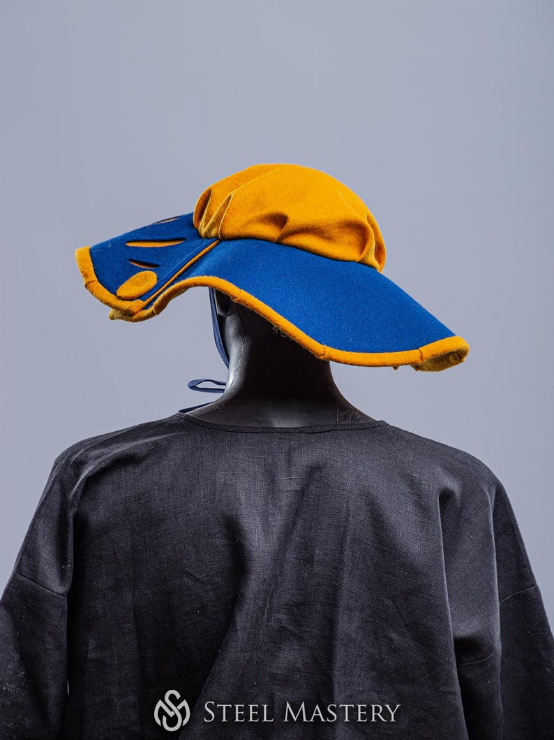 K&ouml;nnte beinhalten: Ein Hut mit breiter Krempe, blauer Krone und gelbem Rand. Der Hut hat ein einzigartiges Design mit Ausschnitten in der Krempe.
