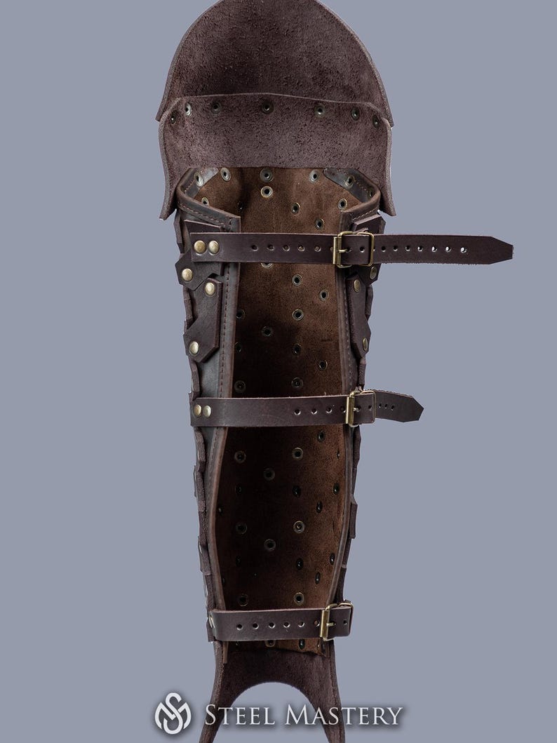 May include: Brown leather leg armor with buckles and straps. The armor is made of multiple pieces of leather that are stitched together. The armor is designed to protect the shin and calf.