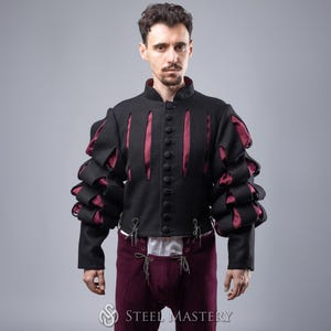 May include: A black doublet with red and black puffed sleeves. The doublet has a high collar and is fastened with buttons. The sleeves are gathered at the elbow and wrist. The doublet is worn over a white shirt and burgundy trousers.