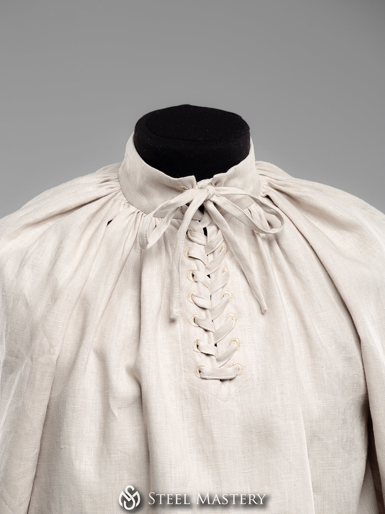 May include: A beige linen shirt with a lace-up neckline. The shirt has a gathered, puffed look around the neckline.