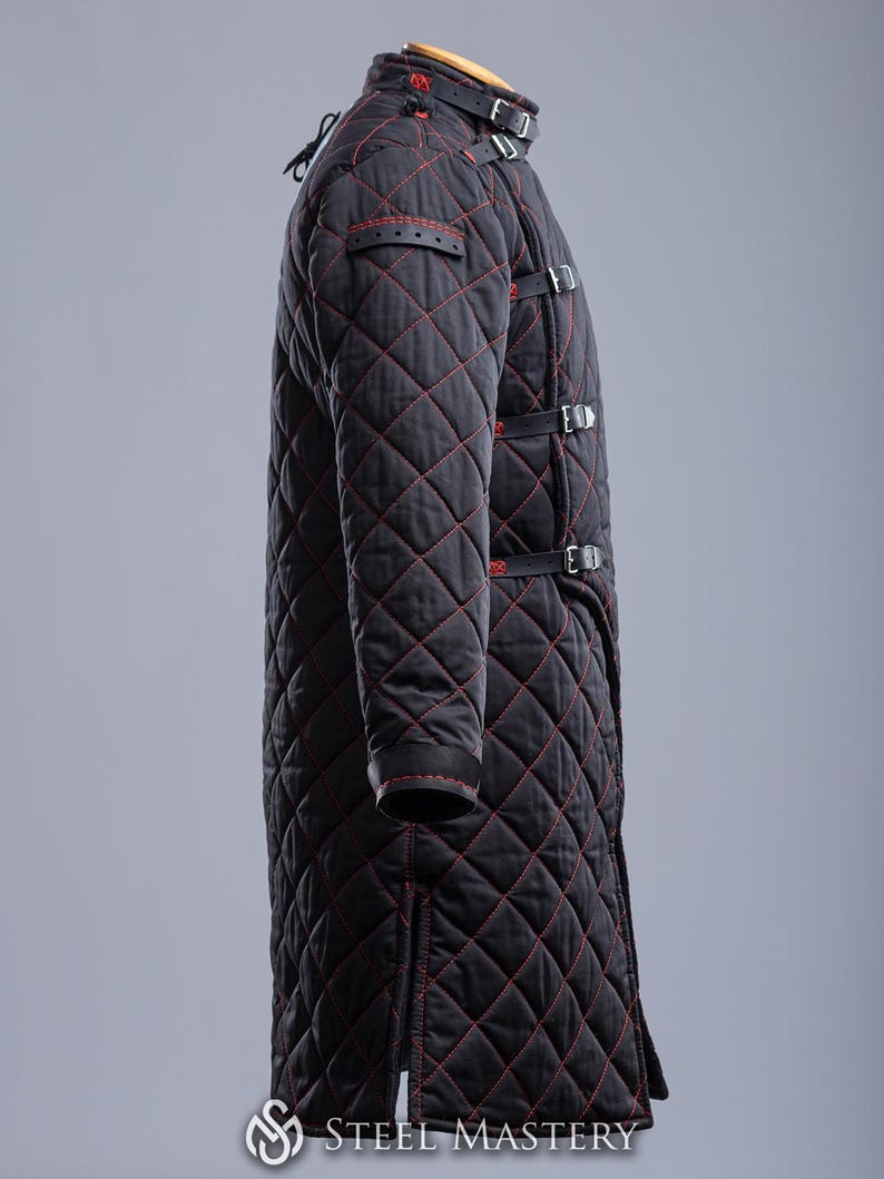 May include: A black quilted coat with red stitching and leather straps. The coat has a high collar and is fastened with buckles. The coat is designed for protection and warmth.