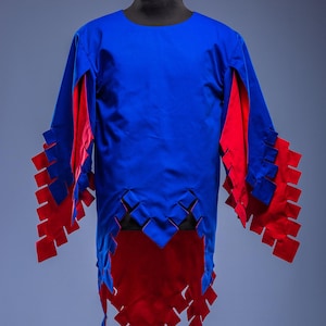 May include: A blue and red tunic on a mannequin. The tunic features a round neck and long sleeves with red detailing. The hem and sleeves are cut with a geometric pattern. The Steel Mastery logo is at the bottom.