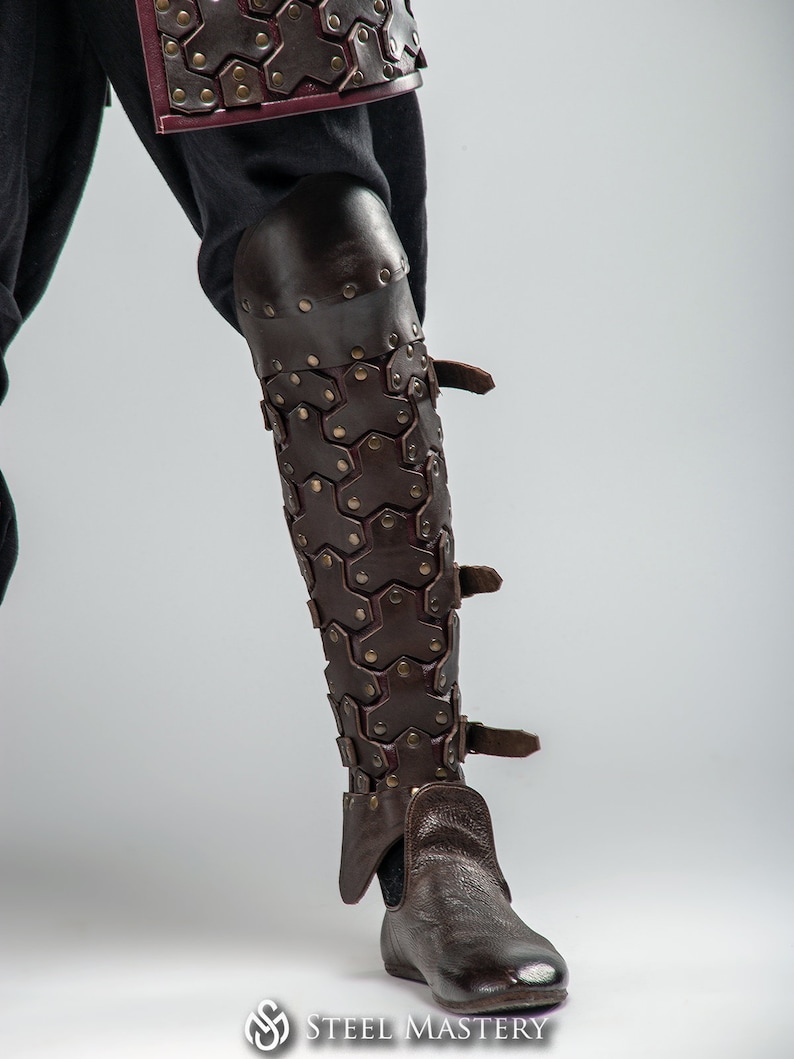 May include: Brown leather leg armor with a hexagonal pattern and buckles. The armor is worn over a pair of brown leather boots.