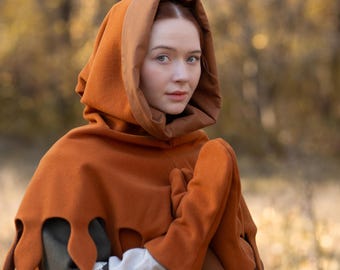 May include: A person wearing a rust-colored hooded cloak with decorative edges and matching mittens. The cloak is layered over a white blouse with lace trim and a rust-colored dress. The logo "STEEL MASTERY" is visible.