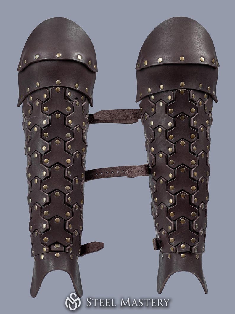 May include: A pair of brown leather arm guards with metal accents and straps. The guards are designed to protect the forearms and elbows.