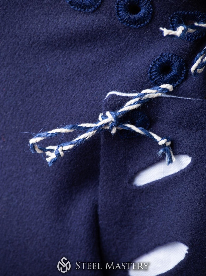 Op de afbeelding: Close-up van een marineblauwe stof met witte en blauwe stiksels. De stof heeft een aantal kleine gaten en een wit koord dat door de gaten is gebonden.