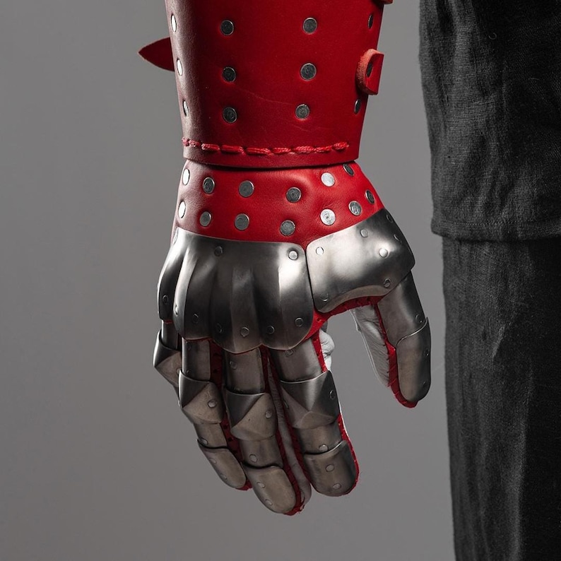 May include: A red leather gauntlet with silver metal plates covering the hand and fingers. The gauntlet is studded with silver rivets and features a red leather cuff. The design suggests medieval armor.