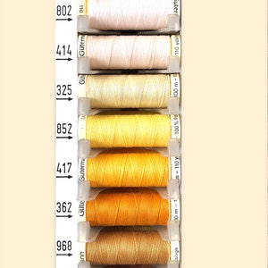May include: A range of thread spools in shades of yellow, orange, and brown, displayed vertically. Each spool is labelled with a number and brand name. The thread is wound on plastic spools.