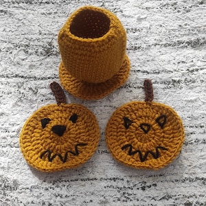 Puede incluir: Conjunto de artículos de ganchillo con temática de calabaza hechos a mano. El conjunto incluye dos posavasos redondos con caras de jack-o'-lantern y un pequeño soporte cilíndrico. Los artículos están hechos de hilo amarillo mostaza con acentos marrones.