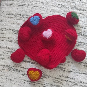 May include: A red crocheted heart-shaped blanket with eight smaller crocheted hearts in various colors, including red, pink, blue, and green.