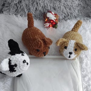 May include: Three crocheted plush dog toys. One is brown, one is tan with white accents, and one is black and white.